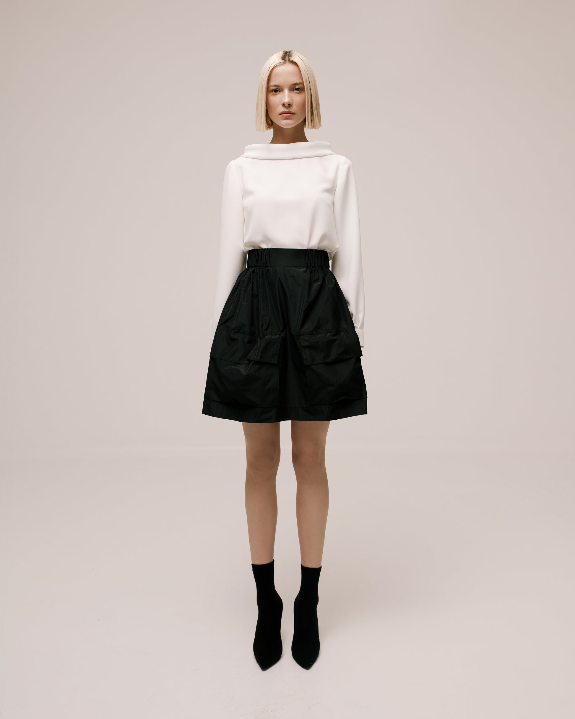 Model wears the Amelia Toro Gathered Taffeta Mini Skirt in Black, front view