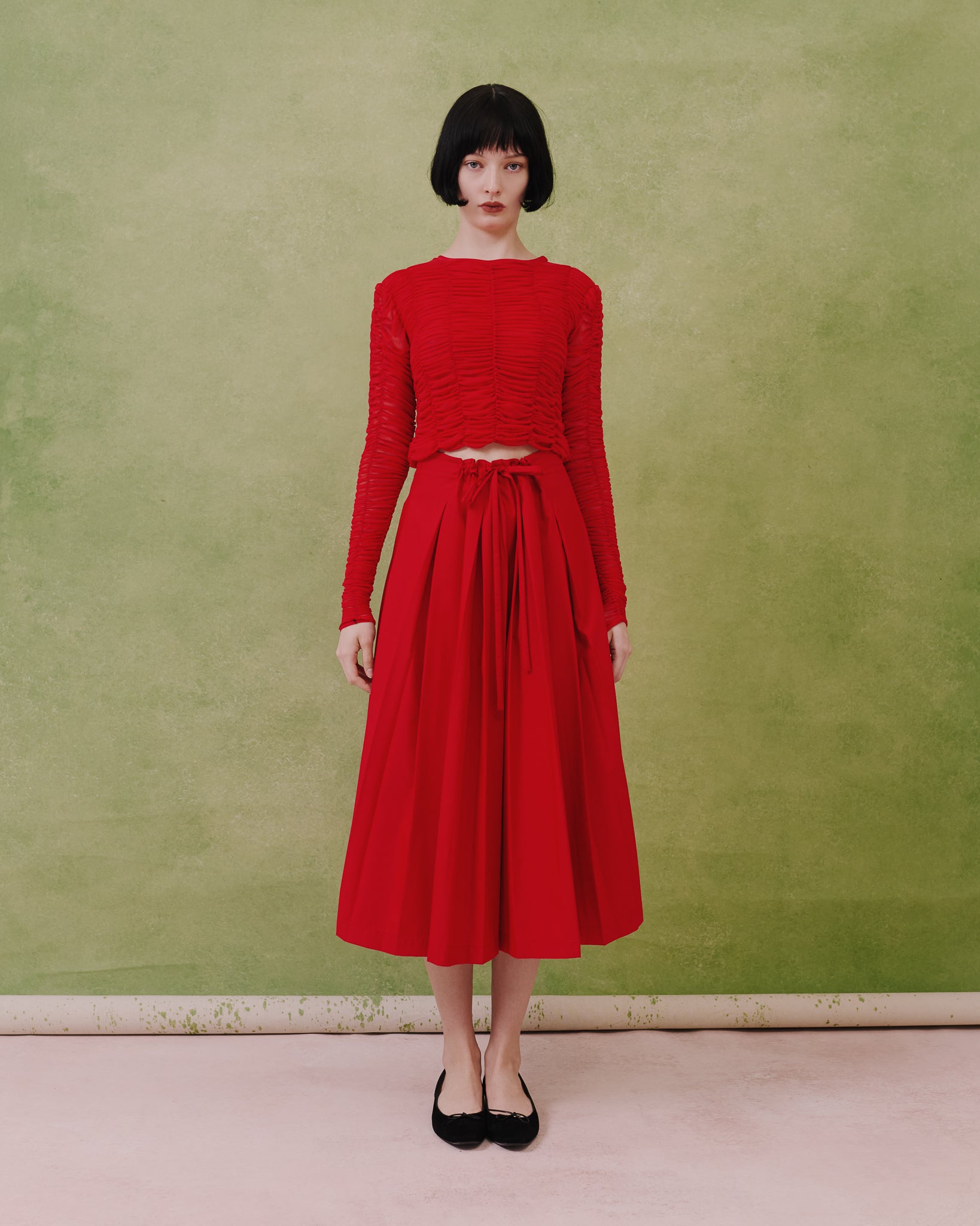 Model wears the Amelia Toro Gathered-Waist Pleated Midi Skirt in red, front view