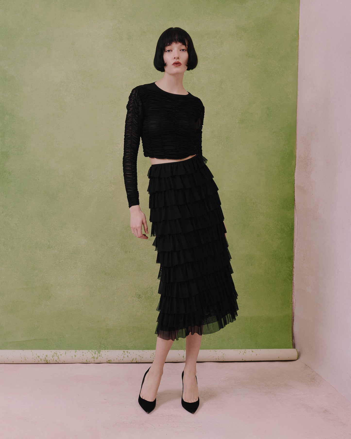 Model wears the Amelia Toro ruched tulle long-sleeve crop top in black with a tiered ruffle skirt, front view