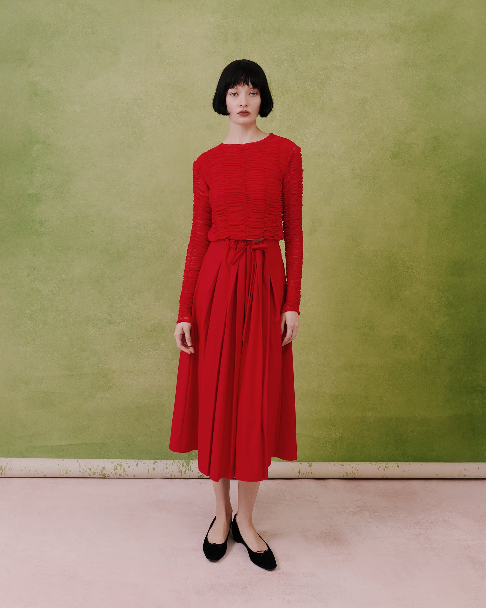 Full-length view of the Amelia Toro ruched tulle long-sleeve crop top in red with a pleated midi skirt
