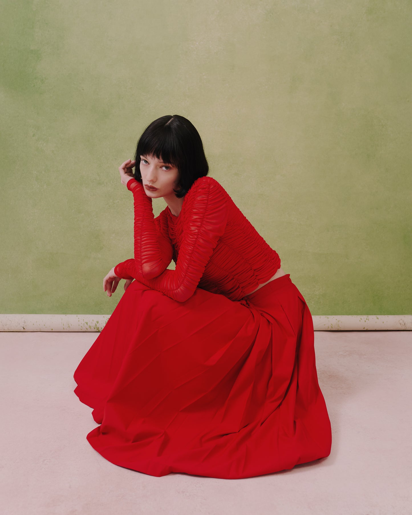 Model seated in the Amelia Toro ruched tulle long-sleeve crop top in red, showing the ruched sleeves