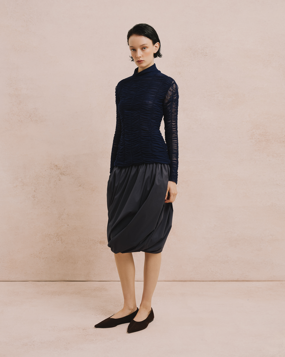 Model wears the Amelia Toro Ruched Tulle Turtleneck Top in blue, styled with a charcoal balloon skirt, front view