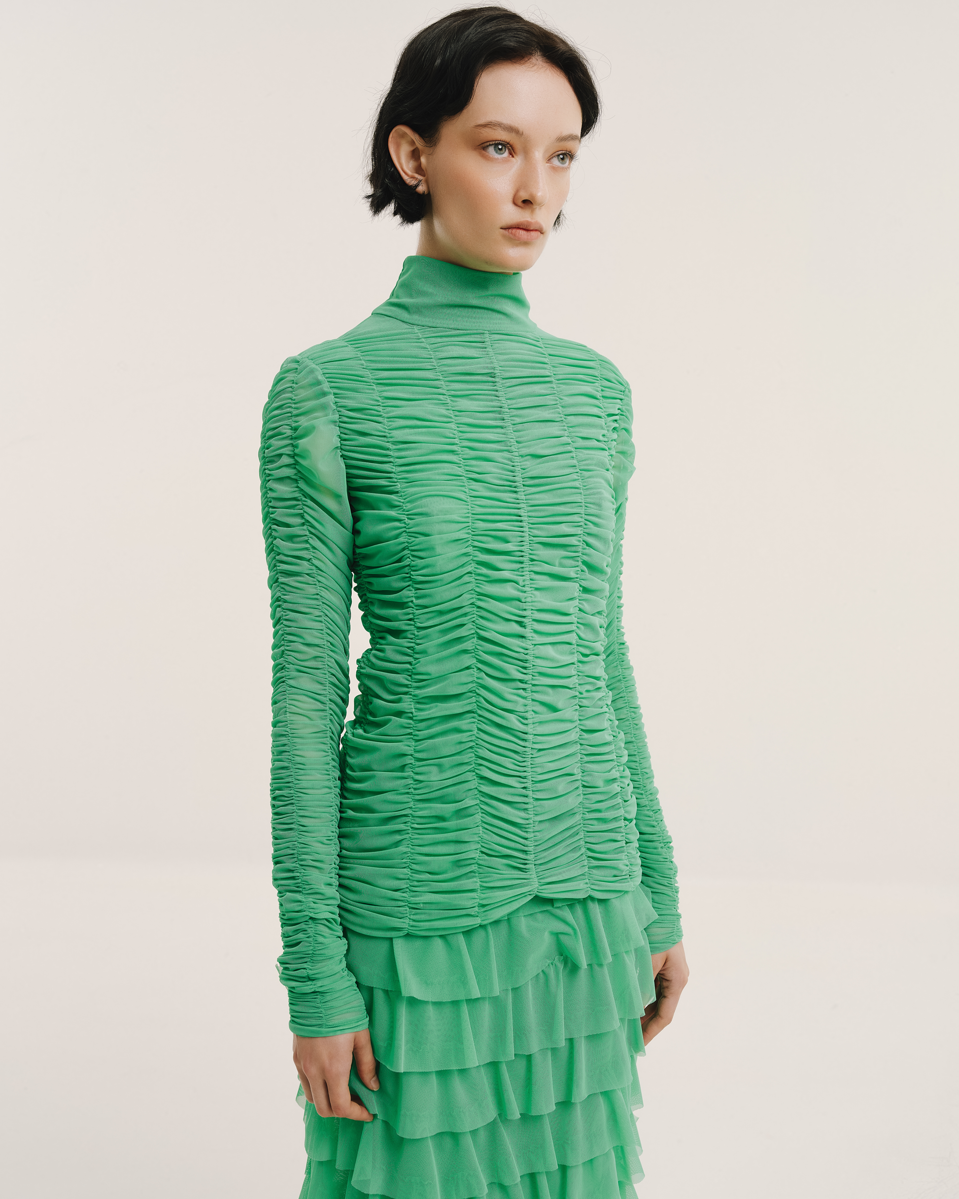 Model wears the Amelia Toro Ruched Tulle Turtleneck Top in green mint, styled with a green ruffled skirt, front view