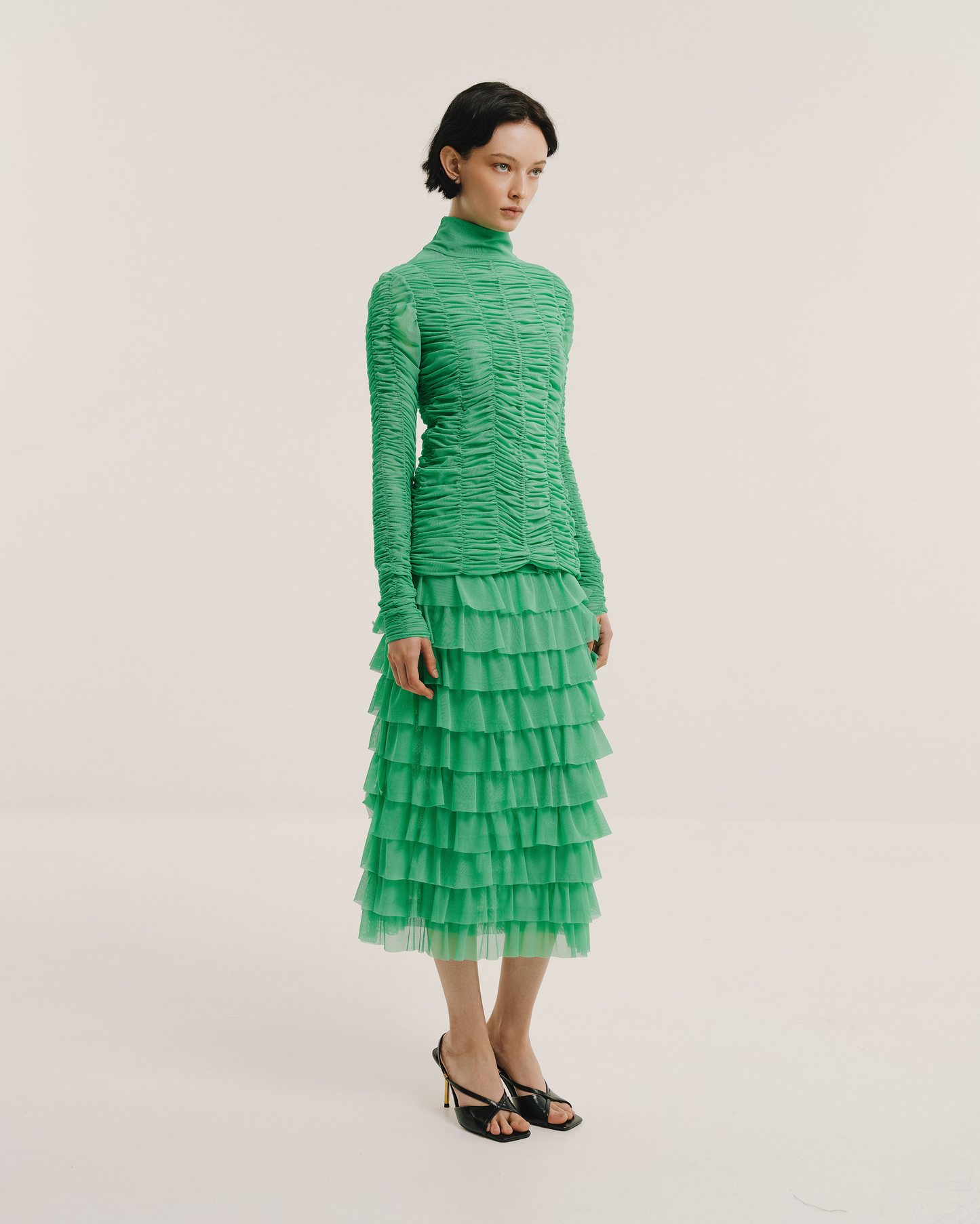 Model wears the Amelia Toro Ruched Tulle Turtleneck Top in green mint, styled with a green ruffled skirt, front view