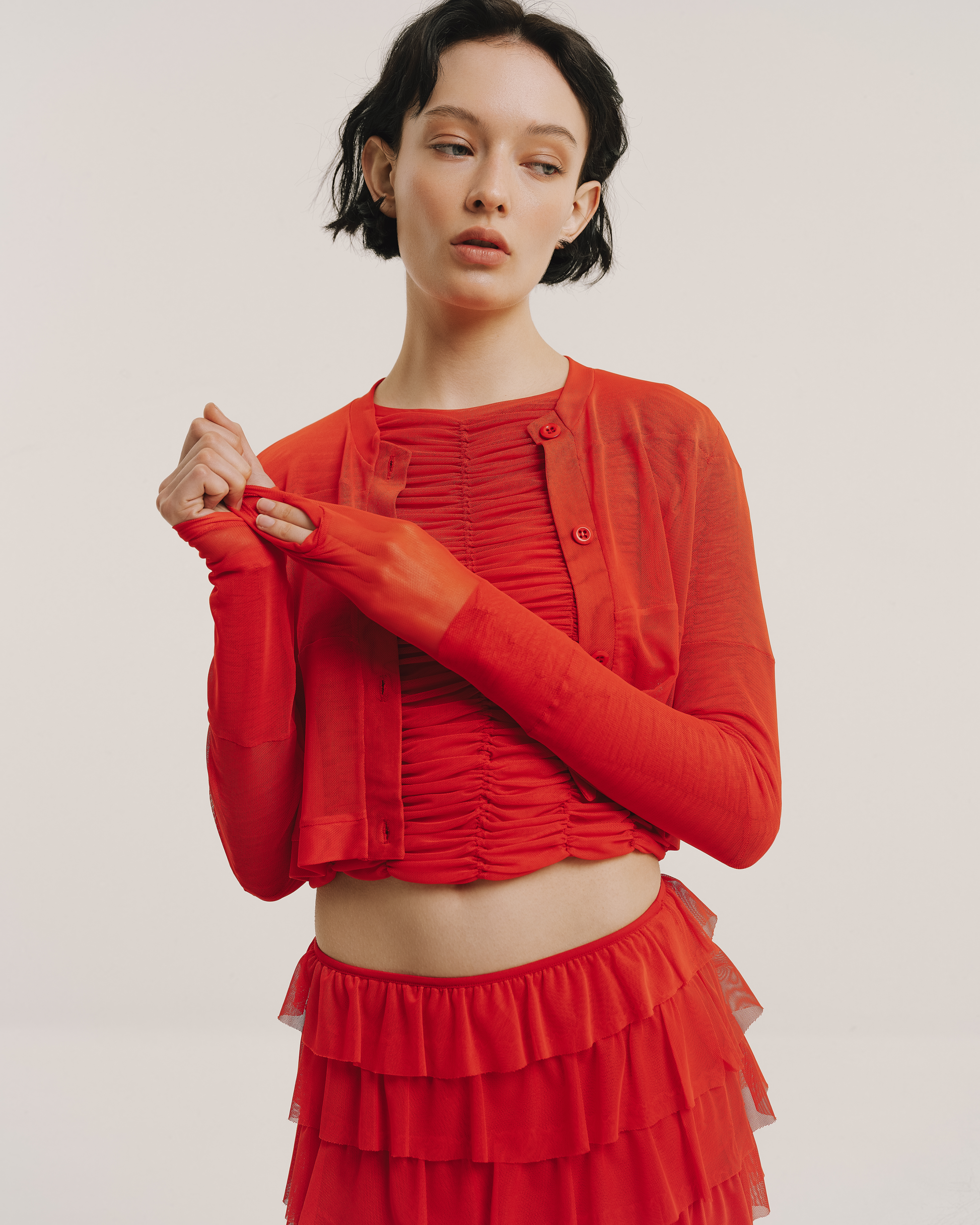Model wears the Amelia Toro Sheer Tulle Cropped Sweater in red, front view
