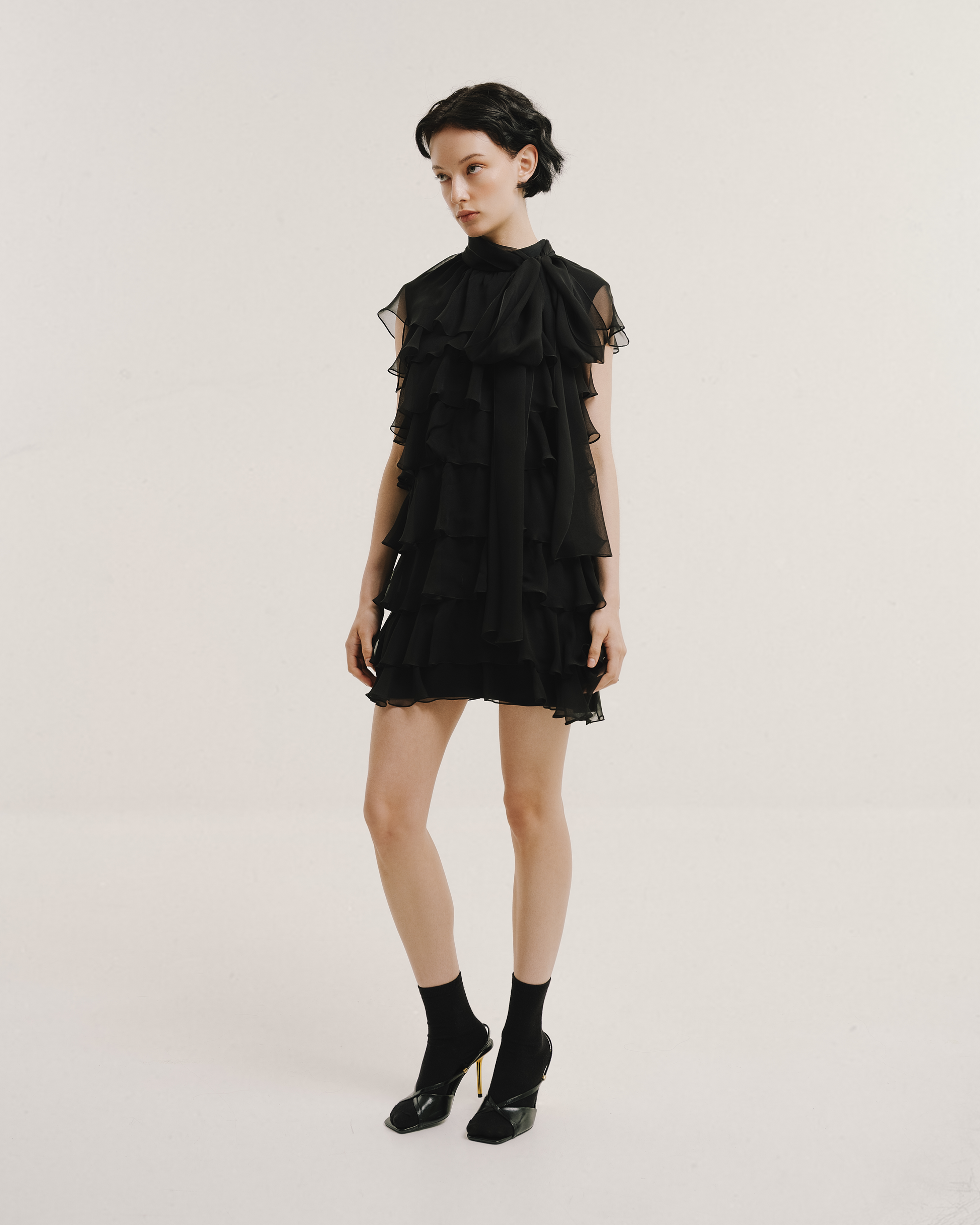 Model wears the Amelia Toro Silk Chiffon Tiered Ruffle Mini Dress in black, front view